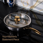 Stainless steel frying pan with gold handle on a black stovetop, text 'Your Kitchen's Statement Piece' below.