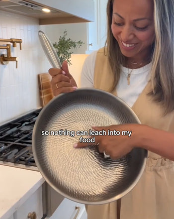 A woman in a kitchen holds up a hammered stainless steel pan, pointing to the textured interior with the text 'so nothing can leach into my food.